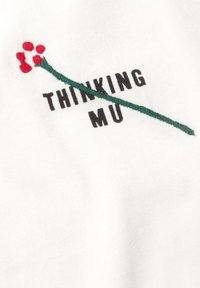 Weißes T-Shirt aus Stoff mit einem grünen gestickten Blumenstamm und roten Knopsen sowie schwarzem Text mit der Aufschrift "THINKING MU."