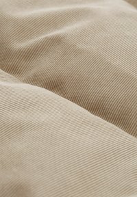 Tejido de sarga color beige con estrías verticales y suaves pliegues que crean sombras suaves y variaciones de textura.