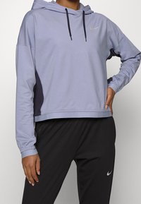 Lichtpaarse hoodie met een capuchon met trekkoord, zwarte zijpanelen en een zilveren Nike-logo op de borst. Getextureerde stof, comfortabele pasvorm.
