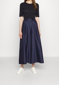 Marinblå satinmaxikjol med veckad design, hög midja och en mjuk textur, kombinerad med en svart kortärmad topp och vita sneakers.