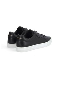Baskets en cuir noir avec une finition lisse, semelle en caoutchouc blanc et un discret logo doré sur le talon. Design classique à lacets.