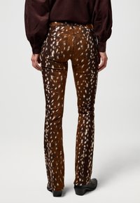 Jeans marroni svasati con una texture a motivo caratterizzata da macchie bianche e una finitura liscia, abbinati a calzature nere. Vita regolare e tasche visibili.