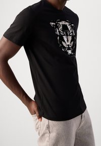 Černé bavlněné tričko s výrazným potiskem tygří tváře v bílé barvě. Krátké rukávy a kulatý výstřih. Pohodlný střih.