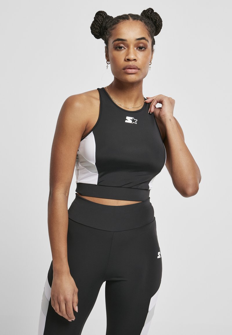 Musta urheilullinen crop-top valkoisilla sivupaneeleilla, istuva malli ja logotyyli. Yhdistetty harmaisiin korkeavyötäröisiin legginsseihin. Sileä pinta.