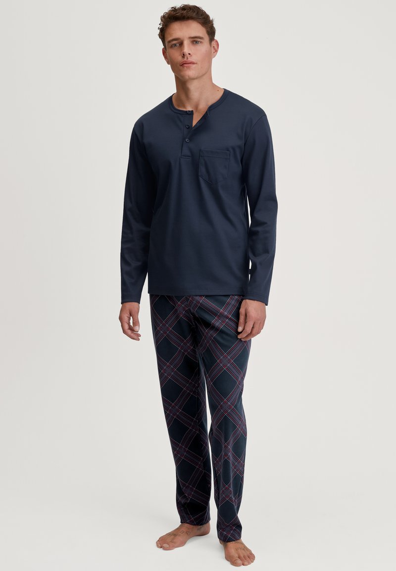 Marineblauwe long-sleeve top met een henley-hals en zak; geruite pyjamabroek in marineblauw, rood en wit; zacht, lichtgewicht stof.