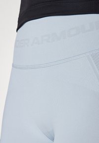 Lyseblå stretchy leggings har en teksturert midje med "UNDER ARMOUR"-merke i en subtil nyanse. Glatt stoff, tettsittende design.