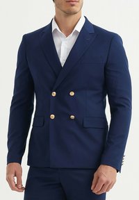 Veste bleu marine à double boutonnage avec boutons dorés, revers à cran, poches latérales et quincaillerie décorative sur les manches. Texture de tissu lisse.
