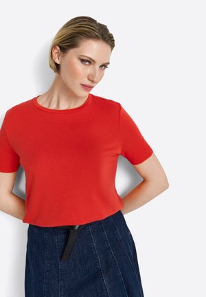 T-shirt rossa a maniche corte con scollatura rotonda, realizzata in tessuto liscio, abbinata a una gonna in denim scuro con un accento in cintura nera.