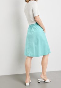 Falda de aqua marina hasta la rodilla con cintura elástica y bolsillos laterales. Hecha de tejido ligero, presenta una textura suave y líneas limpias.