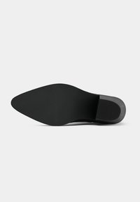Suela de zapato negra con forma puntiaguda, superficie de goma texturizada y un tacón bajo de bloque. Diseños mínimos sin patrones o acentos visibles.