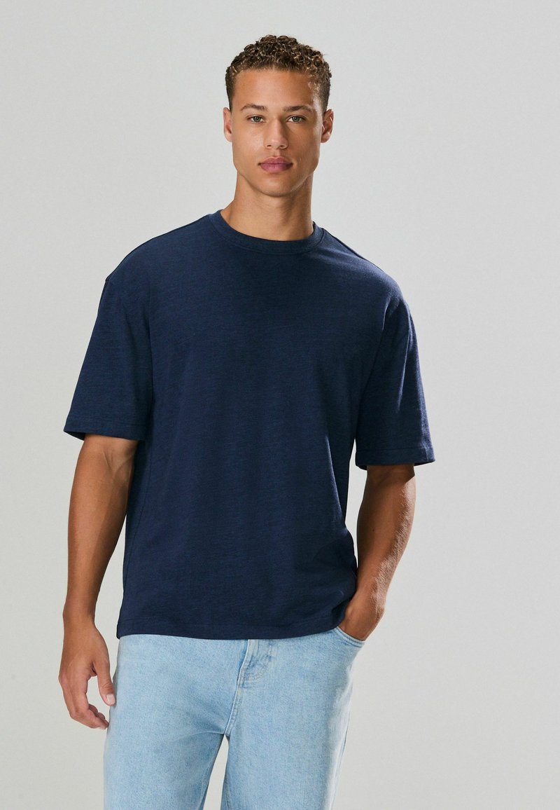 Námorníckomodrá krátkorychlá t-shirt z textúrovanej látky, s okrúhlym výstrihom a voľným strihom, v kombinácii so svetlomodrými džínami.