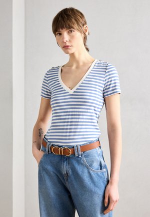 T-shirt à rayures, à manches courtes, de couleur bleu clair et blanc, avec un décolleté en V, des bordures contrastantes et des boutons aux épaules ; associé à un jean taille haute.