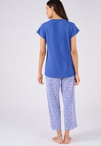 Top de manga corta azul combinado con pantalones blancos que presentan un patrón de hojas azules. La tela parece suave, con un corte recto y un ajuste relajado.