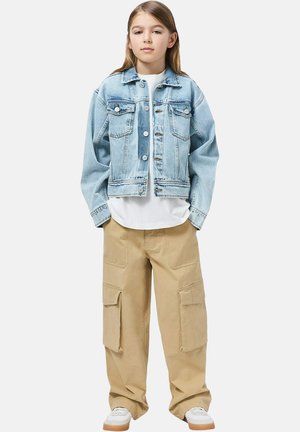 Giacca di denim azzurro chiaro con due tasche sul petto, abbinata a pantaloni cargo beige con multiple tasche e una camicia bianca sotto.