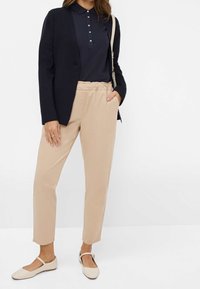 Blazer bleu marine, haut bleu marine à col, et pantalon beige à taille élastique. Ballerines beige clair avec une bride ; texture de tissu lisse partout.