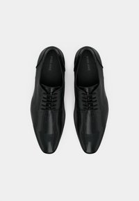 Chaussures habillées noires avec une texture en peau de crocodile, bout pointu et laçage à trois œillets. Finition lisse et brillante avec un marquage subtil à l'intérieur.