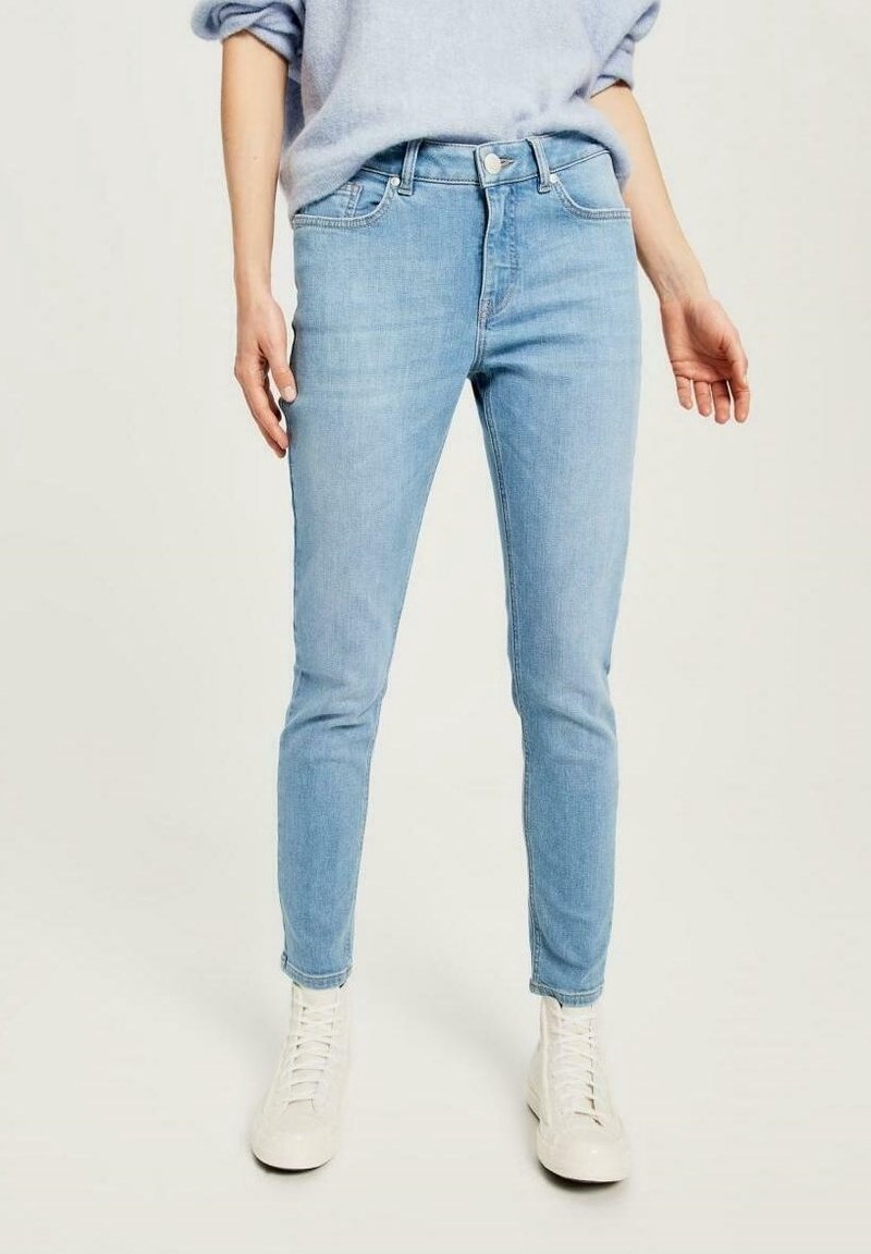 Ljust blå skinny jeans i denim, med hög midja, klassisk femfickdesign och en slät yta. Matchat med vita sneakers.