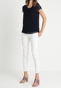 Blusa de manga corta azul marino con frente plisado, combinada con pantalones ajustados blancos y mule de tacón bloque rosa. Tejidos suaves y diseño sencillo.