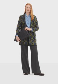 Cardigan en tricot avec un motif floral vert et bleu, pantalon large gris, chemise bleu clair et sac à main noir. Texture lisse, coupe décontractée.