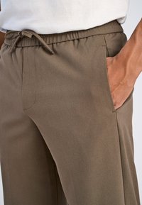 Braune, leichte Hose mit elastischem Bund, Kordelzug und seitlichen Taschen; die Oberfläche ist glatt mit einer dezenten Textur.