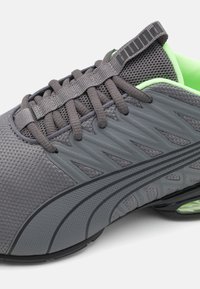 Grå idrottssko med strukturerad syntetisk ovandel, svart och grå sula, vadderad krage i klargul, och snörning med varumärkets dragremsa.