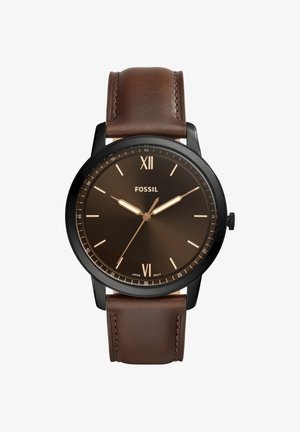 Men's Fossil wristwatch with black round case, brown dial showing 10:10, and brown leather strap with stitching.