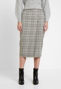 Jupe midi à carreaux en beige, noir et crème ; présente une silhouette ajustée, des boutons sur le côté et une texture lisse. Portée avec des bottines noires.