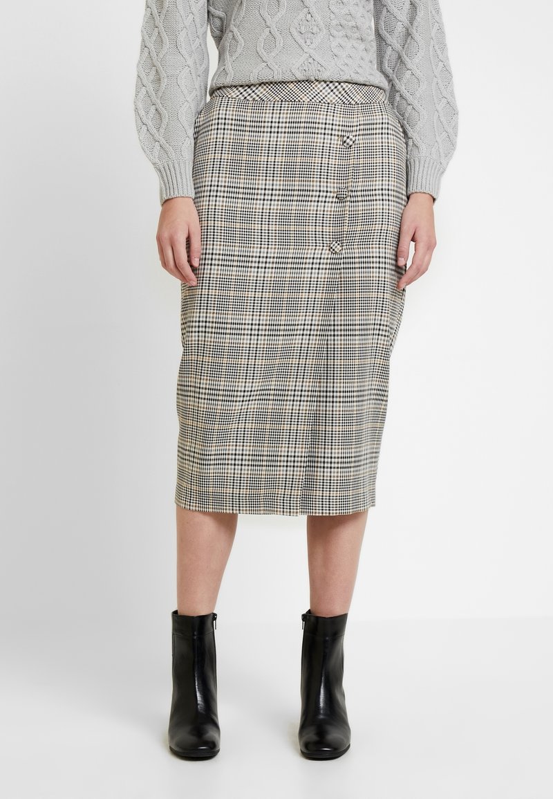 Jupe midi à carreaux en beige, noir et crème ; présente une silhouette ajustée, des boutons sur le côté et une texture lisse. Portée avec des bottines noires.