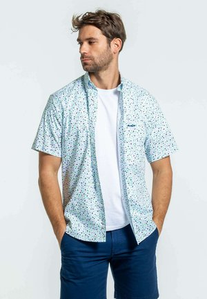 Chemise à manches courtes à boutons de couleur bleu clair avec un motif de pois multicolores, associée à un sous-vêtement blanc et à des shorts navy.