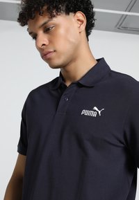Námornícky polo tričko vyrobené z bavlnenej zmesi látky, s preklopeným golierom, krátkymi rukávmi a bielym vyšívaným logom Puma na hrudi.