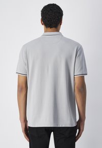 Graues Poloshirt aus Baumwolle mit klassischem Kragen, kurzen Ärmeln und schwarzem Saum an den Ärmelenden. Die Rückansicht zeigt eine einfache, glatte Textur.