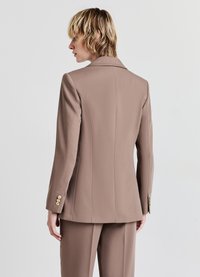 Blazer su misura color marrone chiaro con un taglio moderno, dotato di revers a V, forma aderente e accenti di bottoni dorati sulle maniche.