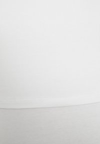 Lähikuva valkoisesta puuvillakankaasta, jossa näkyy ompelujälkiä ja hienoa viistepintaa.