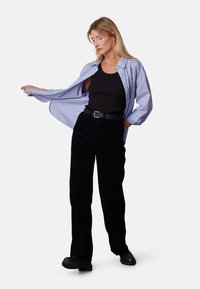 Lichtblauwe button-up shirt, zwarte tanktop, zwarte corduroy wijde broek, zwarte riem en chunky zwarte schoenen; casual pasvorm.