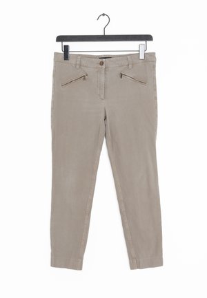 Pantalon beige slim-fit avec poches zippées à l'avant suspendu sur un cintre noir sur fond blanc.
