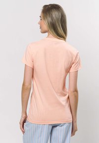 Persikanvärinen lyhythihainen t-paita, jossa pyöreä pääntie ja pehmeä kangas. Päällä sileä pinta ja istuva leikkaus.