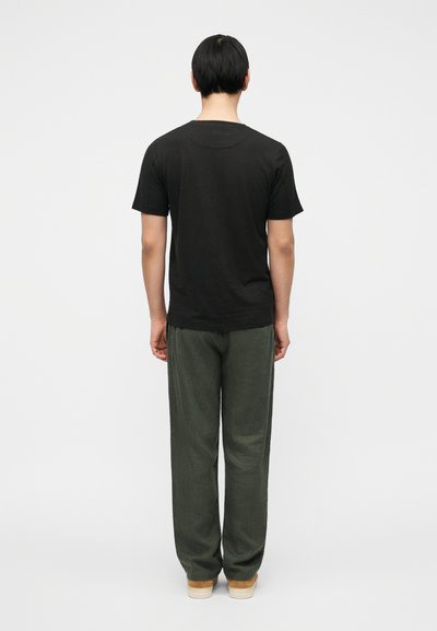 Μαύρο βαμβακερό μπλουζάκι με στρογγυλή λαιμόκοψη, συνδυασμένο με χακί παντελόνι φαρδιάς γραμμής. Το ύφασμα φαίνεται μαλακό και υφασμένο, με casual εφαρμογή.