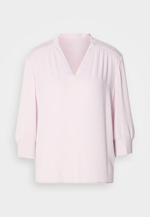 Blouse rose clair à manches courtes avec un col en V, épaules légèrement froncées et coupe décontractée. Texture lisse avec des poignets côtelés.