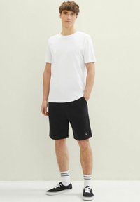 Bílý bavlněný tričko, černé šortky s kapsami a černé tenisky. Doplněno pruhovanými bílými a modrými ponožkami. Ležérní outfit.
