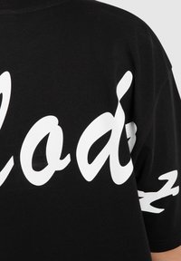 Camiseta de algodón negra con gran texto estilizado en blanco en la parte frontal y detalles estampados en las mangas.