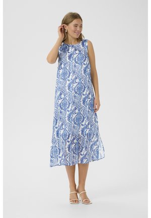 Robe maxi sans manches blanche avec imprimé paisley bleu. Coupe ample, encolure arrondie et fentes latérales. Associée à des sandales à talons blanches.