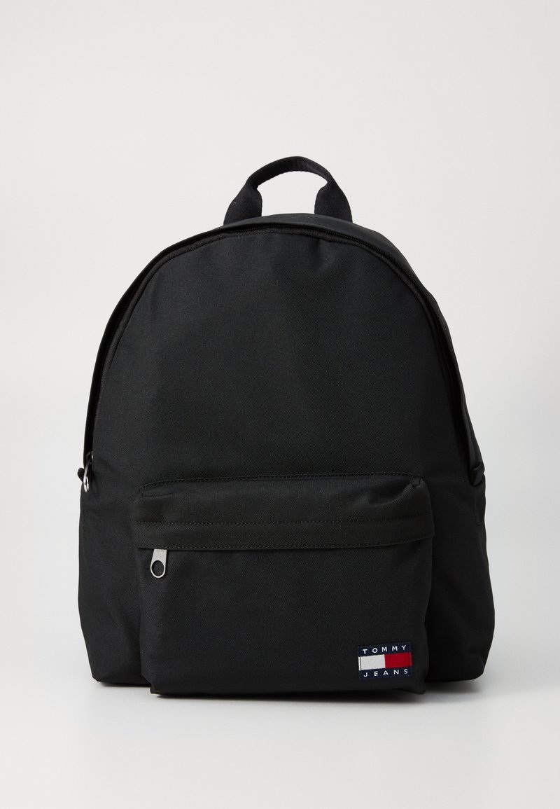Schwarzer Nylon-Rucksack mit runder Form, einer vorderen Reißverschlusstasche und einem Marken-Patch mit blauen, roten und weißen Streifen. Inklusive Tragegriff.