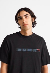 Sort oversized t-shirt med korte ærmer, der har et blåstribet "PUMA" logo og en rød accent af puma-grafikken på brystet.