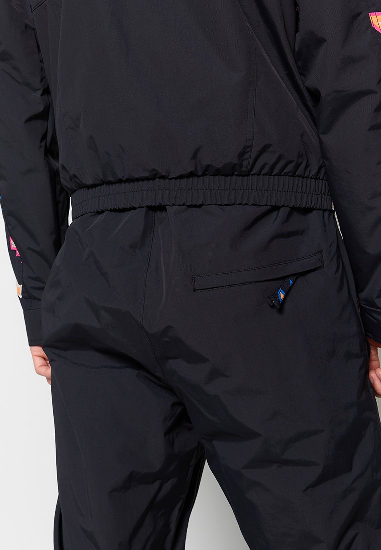 Czarna lekka kurtka z elastycznym pasem, z kolorowymi graficznymi akcentami i zasuwaną kieszenią po prawej stronie.