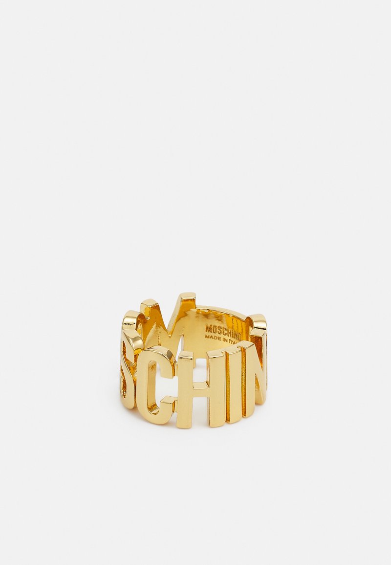 Gold-colored ring featuring bold, cut-out letters spelling "MOSCHINO," with a smooth, reflective finish and a rounded band design.