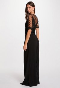 Zwarte jumpsuit met een doorzichtige stippenoverlay, korte mouwen, een getailleerde taille en brede broekspijpen met zijsplitten.
