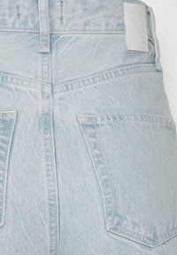 Jeans de denim azul claro com cintura alta, bolsos traseiros e um rótulo de couro simples. Apresenta uma textura suave e costura clássica.