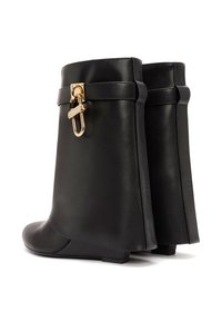 Bottines en cuir noir à semelle plate, avec un accent de boucle dorée et des détails de couture le long des bords.