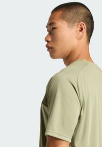 Camiseta deportiva de manga corta en color verde oliva, hecha de un tejido suave y transpirable. Presenta un corte relajado y cuello redondo, con un sutil detalle en las costuras.