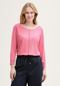 Top roz cu mâneci lungi și decolteu rotund, prezentând un detaliu cu cusătură centrală. Asortat cu pantaloni bleumarin cu șnur, evidențiind o croială lejeră.